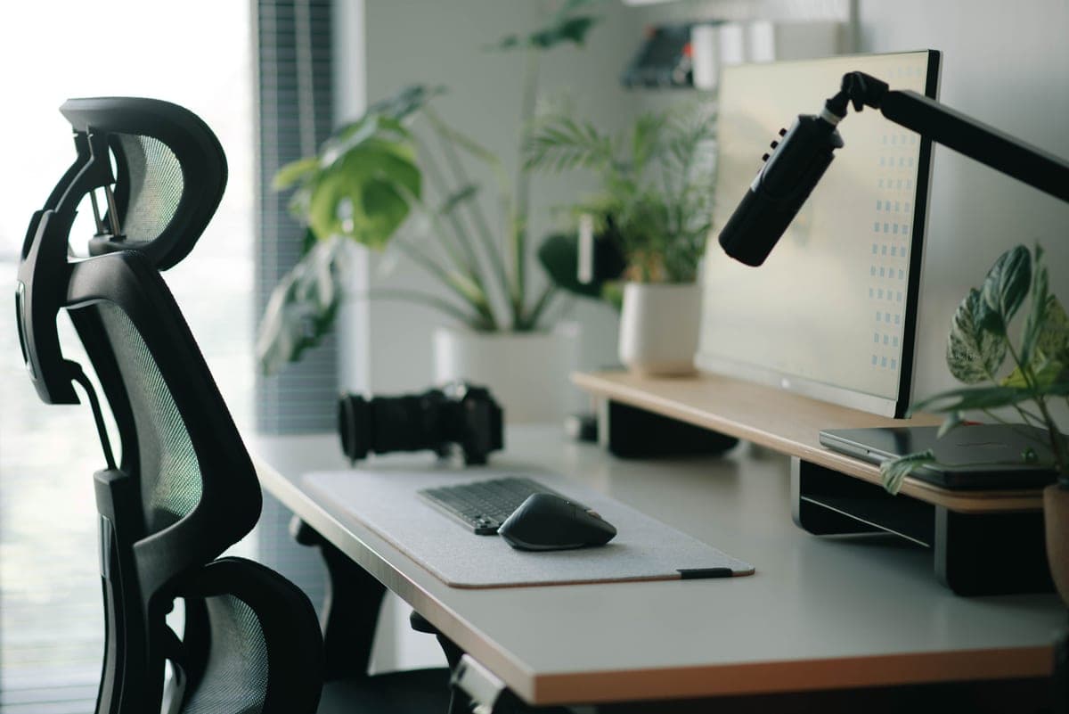 A mesh task chair at a wooden desk in a bright room, seat pan set low, daylight from a side window