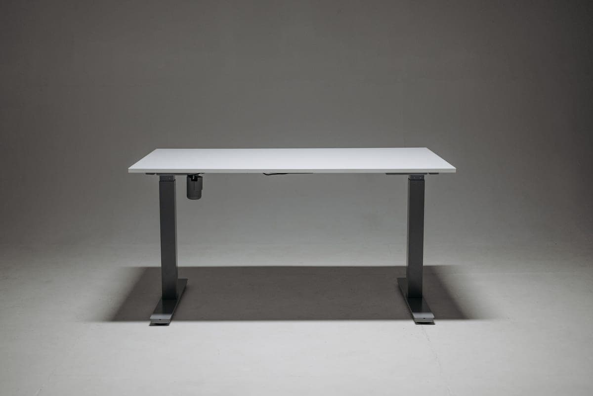 A sit-stand desk raised to standing height in a home office, lit by a window to the left