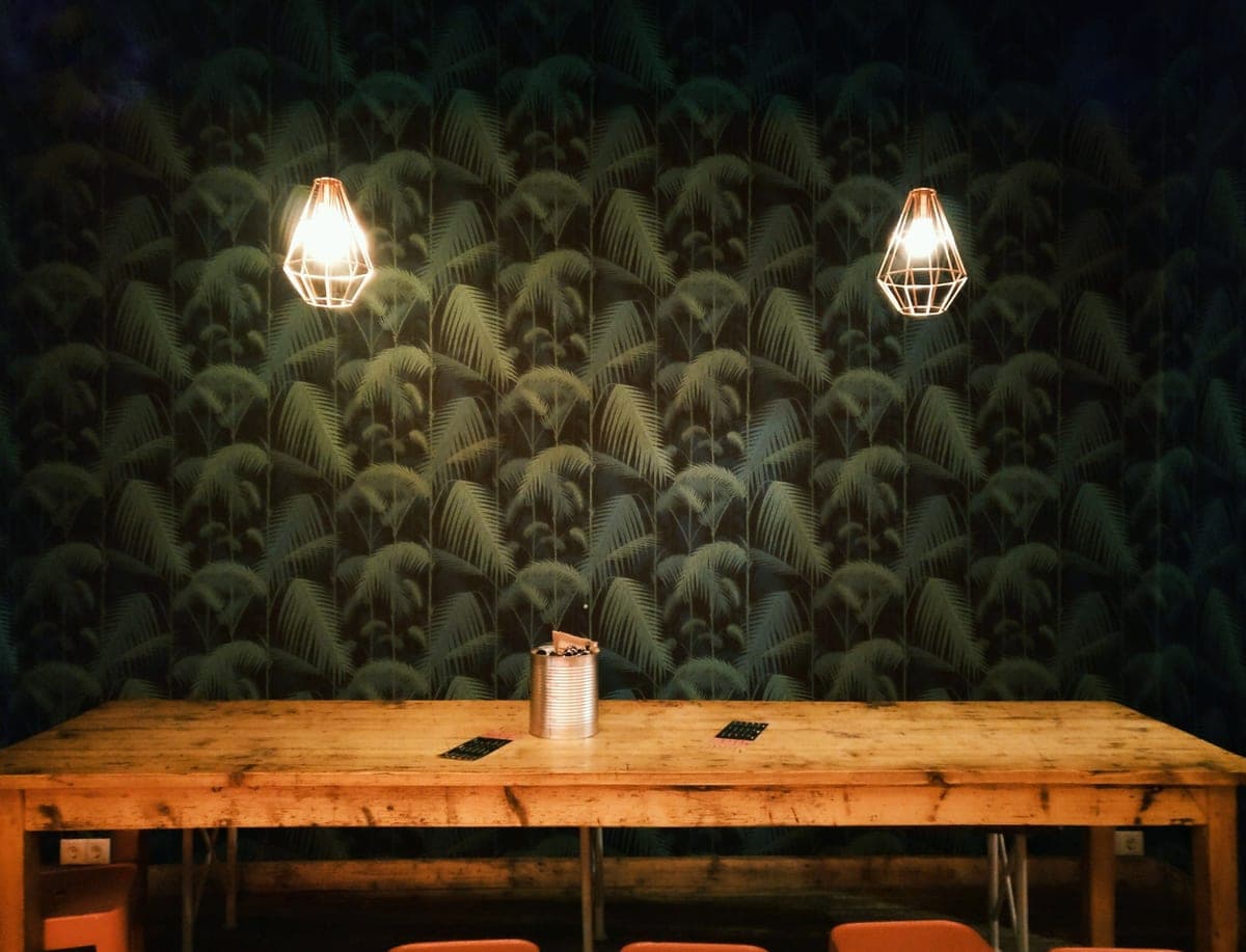 A desk lamp casting warm light across a wooden desk beside a window at dusk