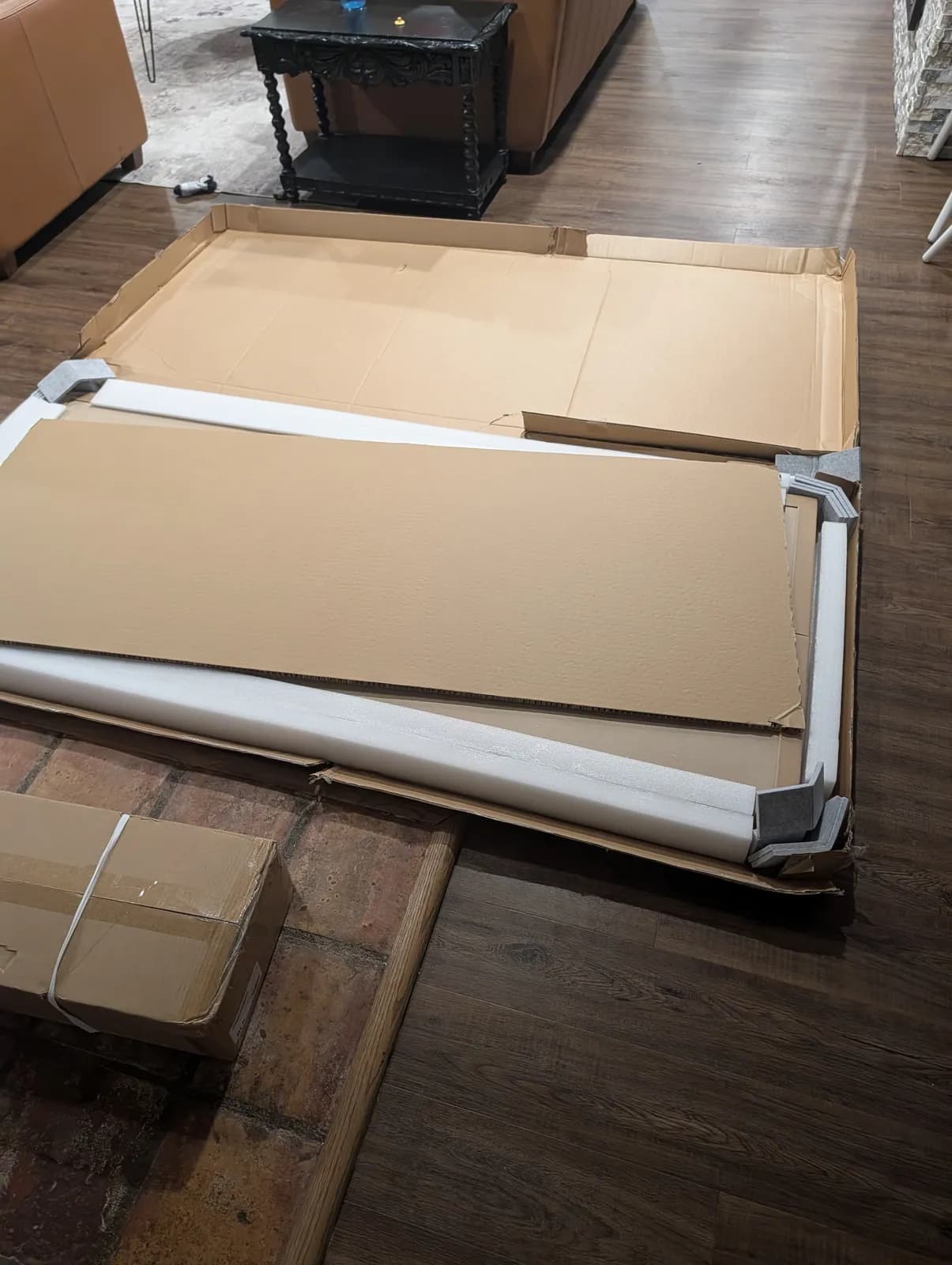 The desktop's flat shipping box opened on the floor, the top still inside between full-length white edge foam and gray foam corner guards.