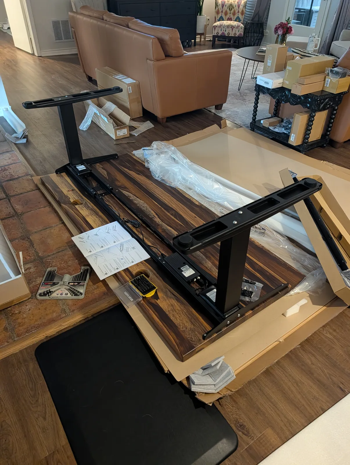 The black V3 C-frame upside down on the underside of the Pheasantwood top, legs and feet attached, hardware and printed instructions laid out around it.
