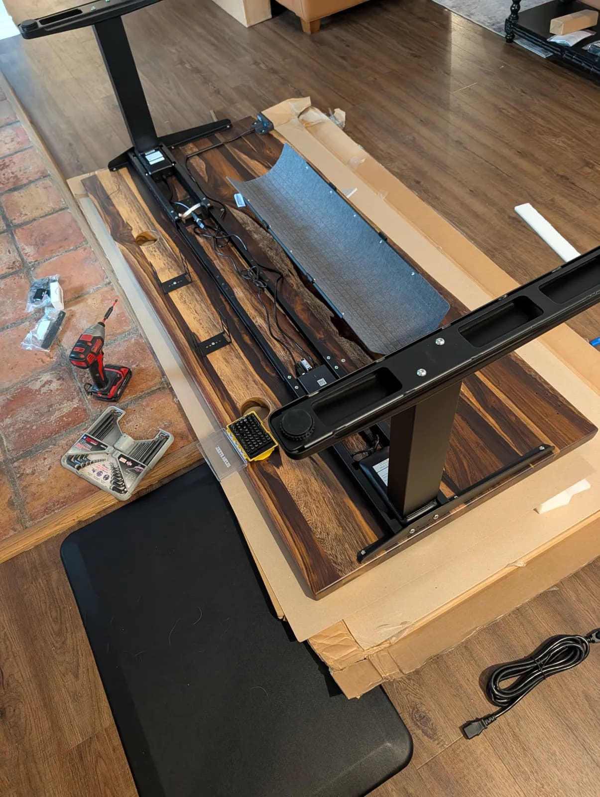 Mid-assembly: the frame's crossbar and cable management bolted to the upside-down top, with a cordless driver and a hex bit set on the floor alongside.