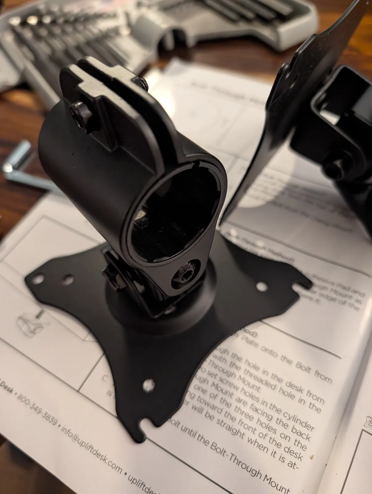 An arm collar and its VESA plate standing on the printed bolt-through mount instructions, with the insert seated in the collar bore.
