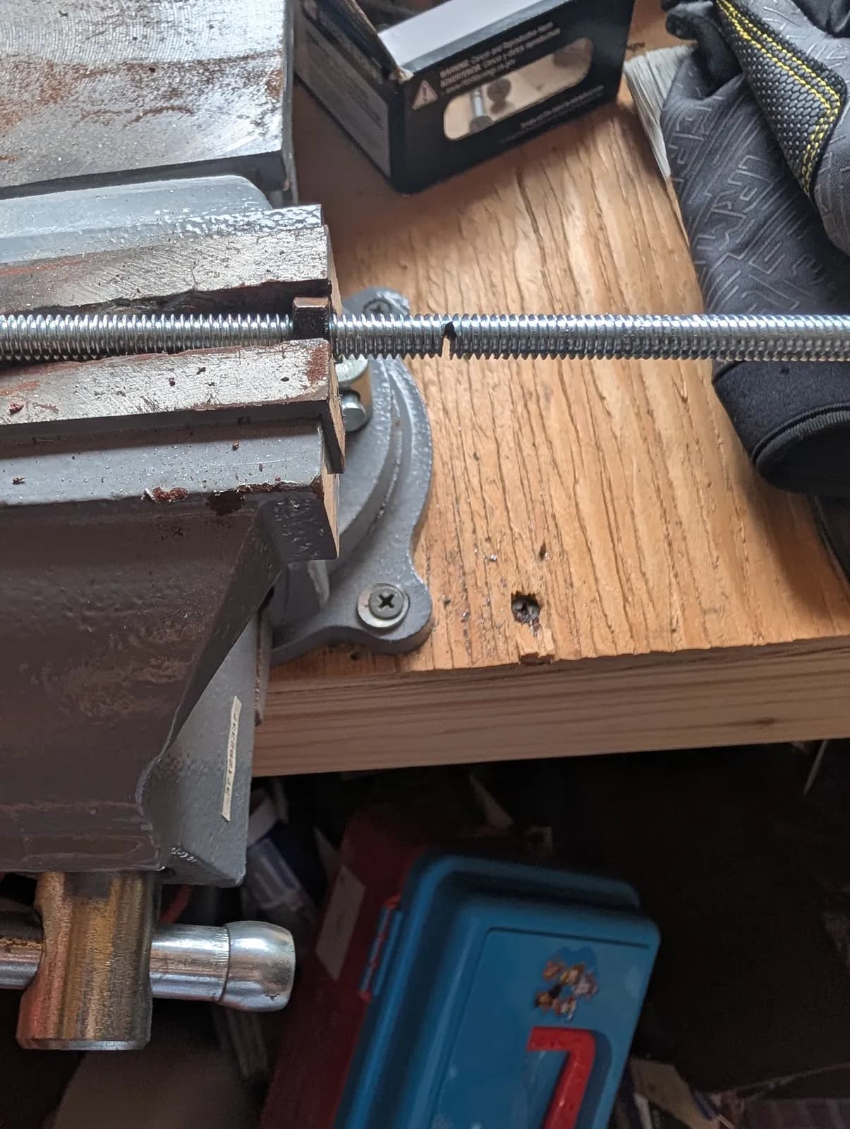The all-thread rod clamped in a bench vise, part-way through being cut to length with a hand cutter.