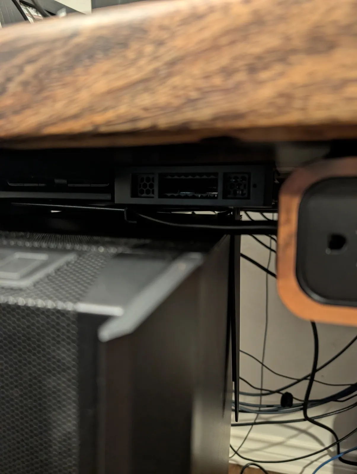 Looking up at the top of the tower under the desk: a spare gray Dell workstation drive wedged between the case and the CPU holder's track as a spacer, with the cut all-thread rod running across above it.