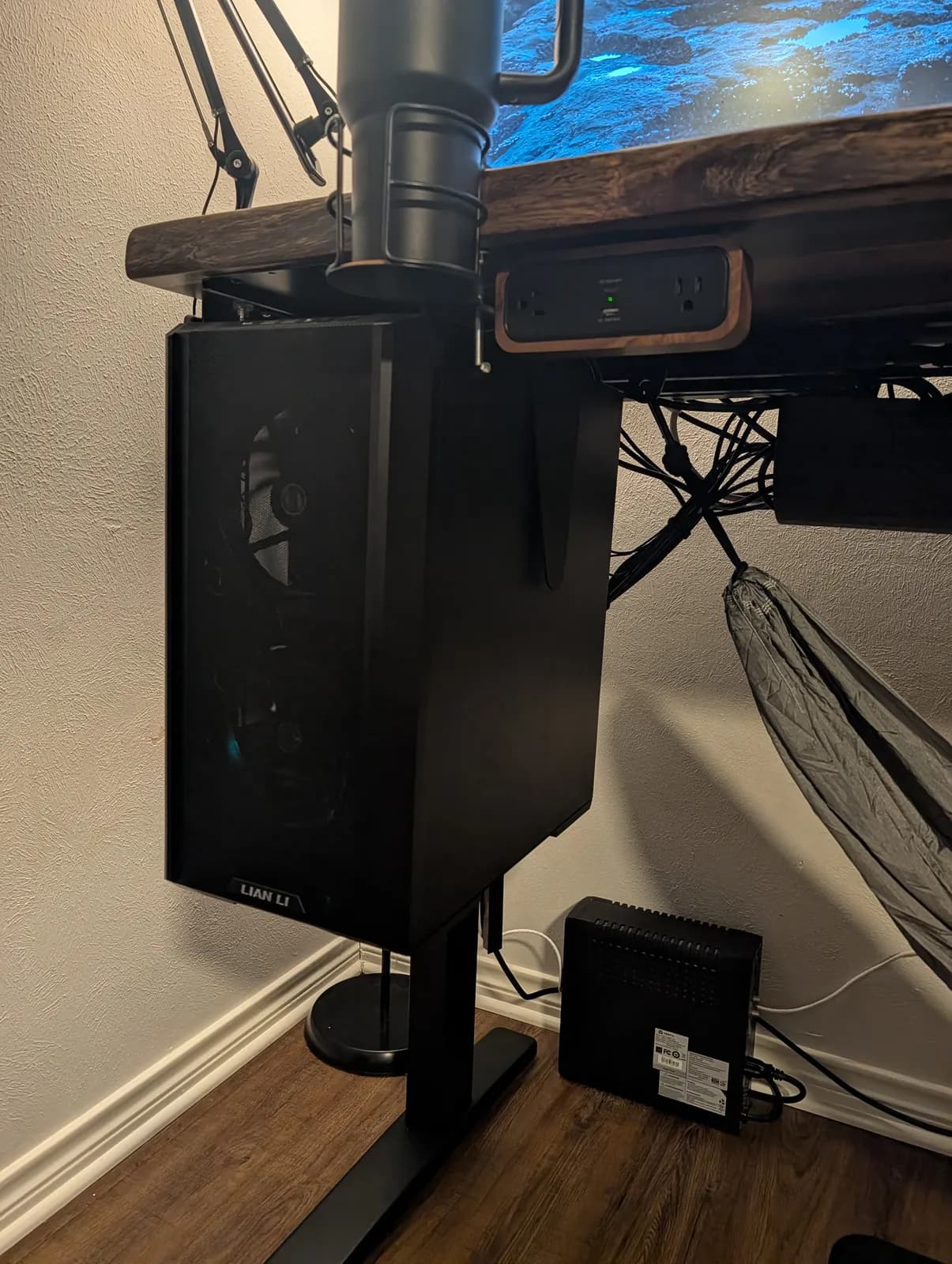 The tower hanging on the CPU holder beneath the left of the desk, with the DuoMount power strip and its walnut accent clamped to the front edge above it.