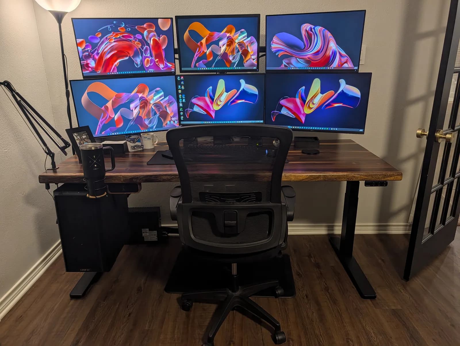 The same six-monitor setup lowered to sitting height, with a mesh task chair pulled up to it on a chair mat.
