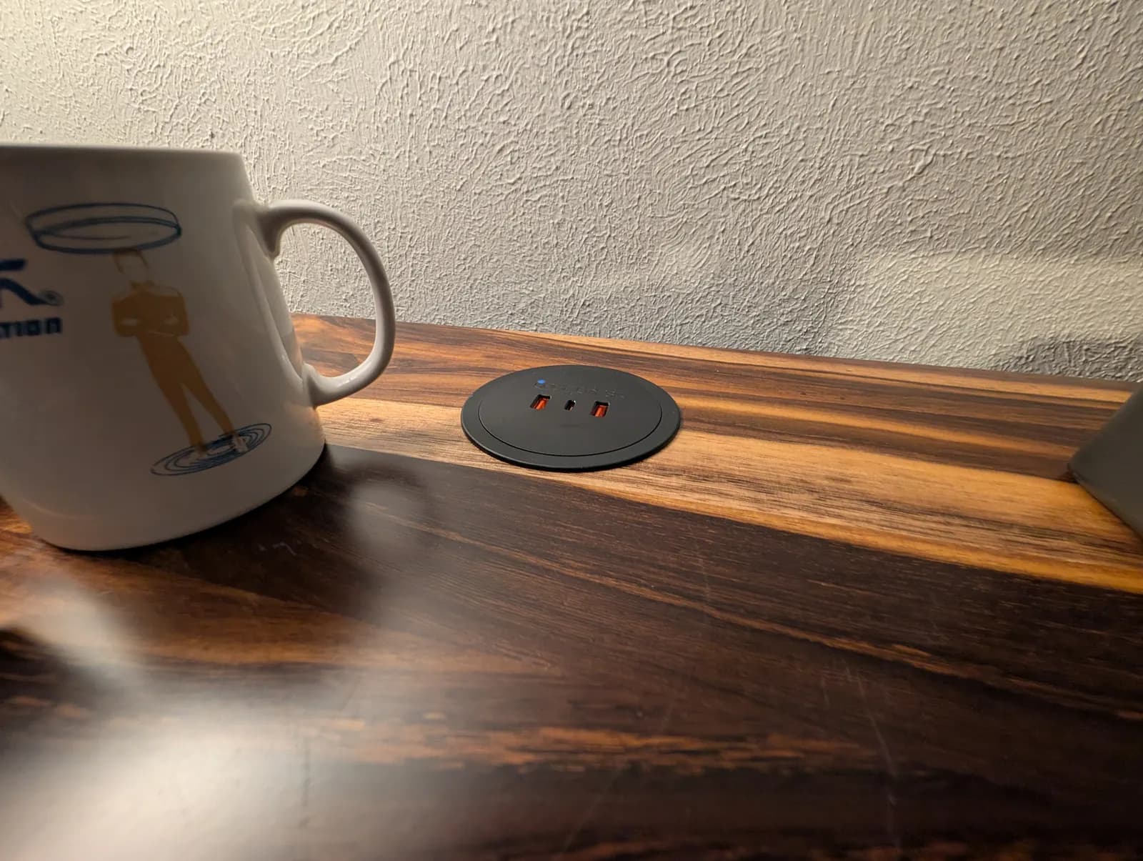 The pop-up power grommet closed, its lid sitting nearly flush with the wood of the desktop next to a mug.