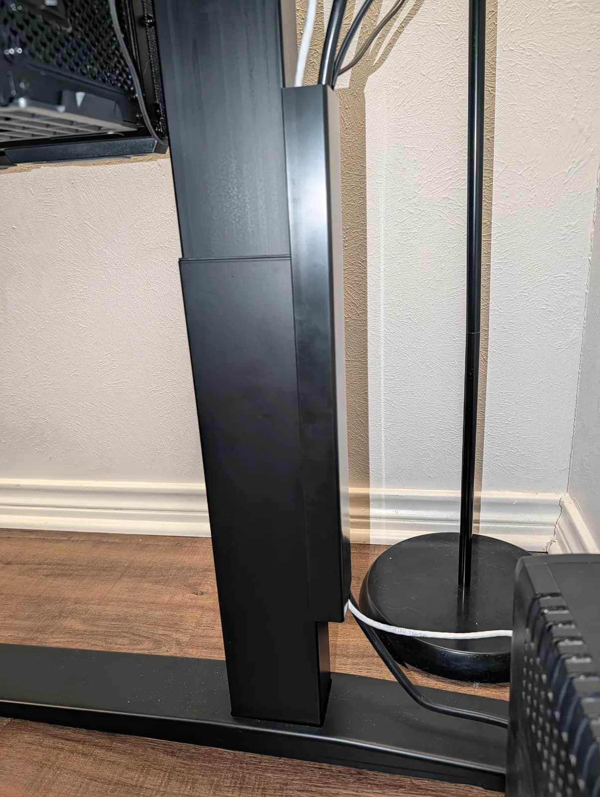 Close-up of one black three-stage leg and its foot on the floor, with cables running up the back of the column.